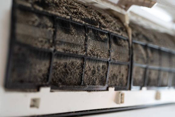 Specialist deep cleaning services Dusty air conditioner filter showing accumulated dirt and debris in the mesh grid