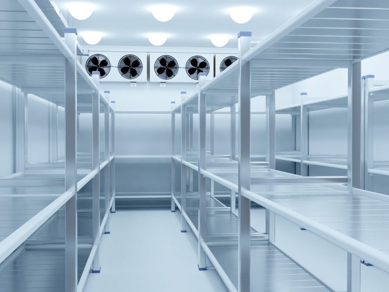 Extenive wrap around provisioning Empty clean chilled storage room with metal shelves and overhead evaporator units.