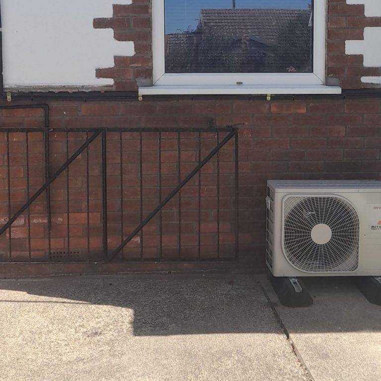 Split system outdoor unit placement A brick wall with a window, metal gate, and an air conditioning unit on the ground.