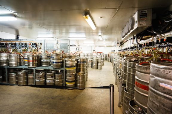 Beer cellar cooling A brewery storage area filled with stacked beer kegs and metal shelves.