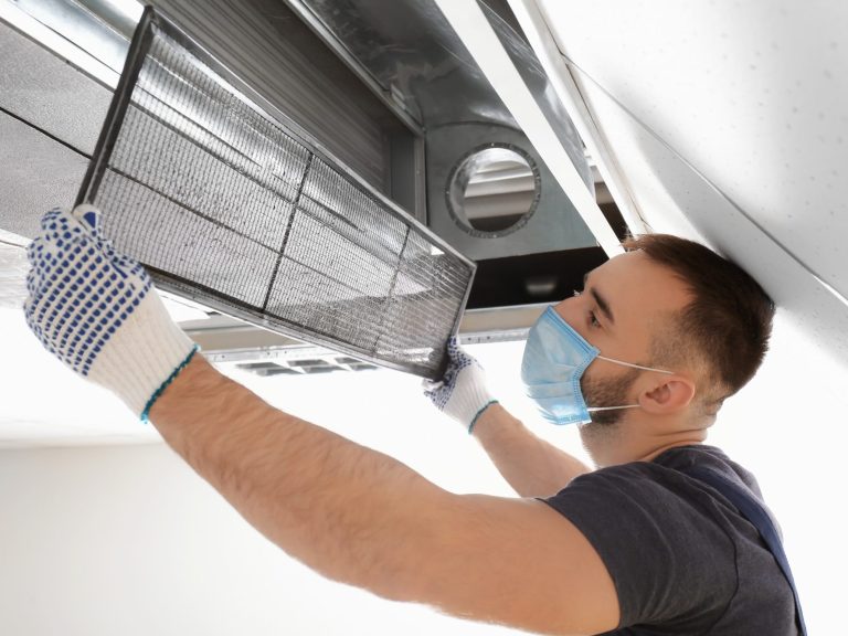 Reliable service, maintenance and repair A technician cleaning an air conditioning unit filter while wearing gloves and a mask.
