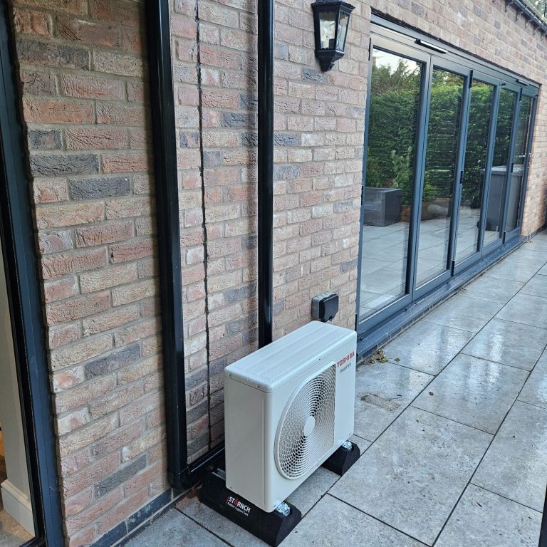 Split system outdoor placement Outdoor air conditioning unit beside a brick wall and large windows on a patio.